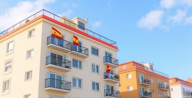 Imagen de un edificio de apartamentos en una zona costera de Galicia con banderas españolas y carteles de alquiler turístico en las ventanas